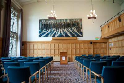 wood-panelled room set out with seating in rows. A large painting hangs on the wall in the backgroung